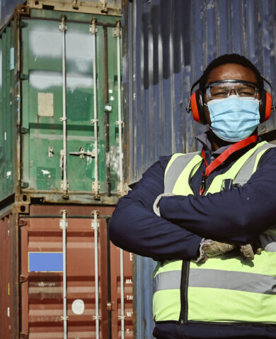 A man assessing and accounting for shipping containers in a storage yard in Johannesburg South Africa. He is wearing a reflective vest and a face mask.