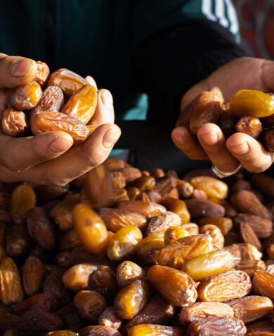 Two hands each holding a handful of dates over a basket filled with dates.