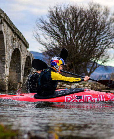 Kayaker paddles along river under a bridge