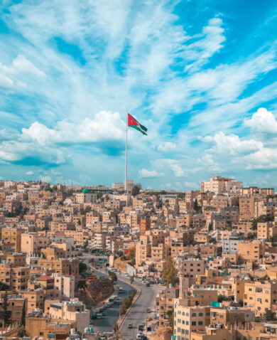 A panoramic view of Amman with a Jordanian flag raised in the middle. 