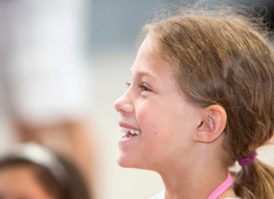 An older elementary girl smiles up at her teacher who is teaching off screen.