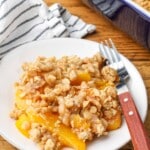 small white plate holding peach crisp with wooden fork