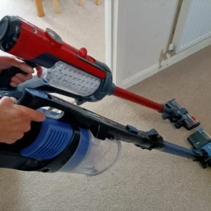 Red Henry Quick cordless vacuum cleaner next to a blue Shark cordless vacuum cleaner