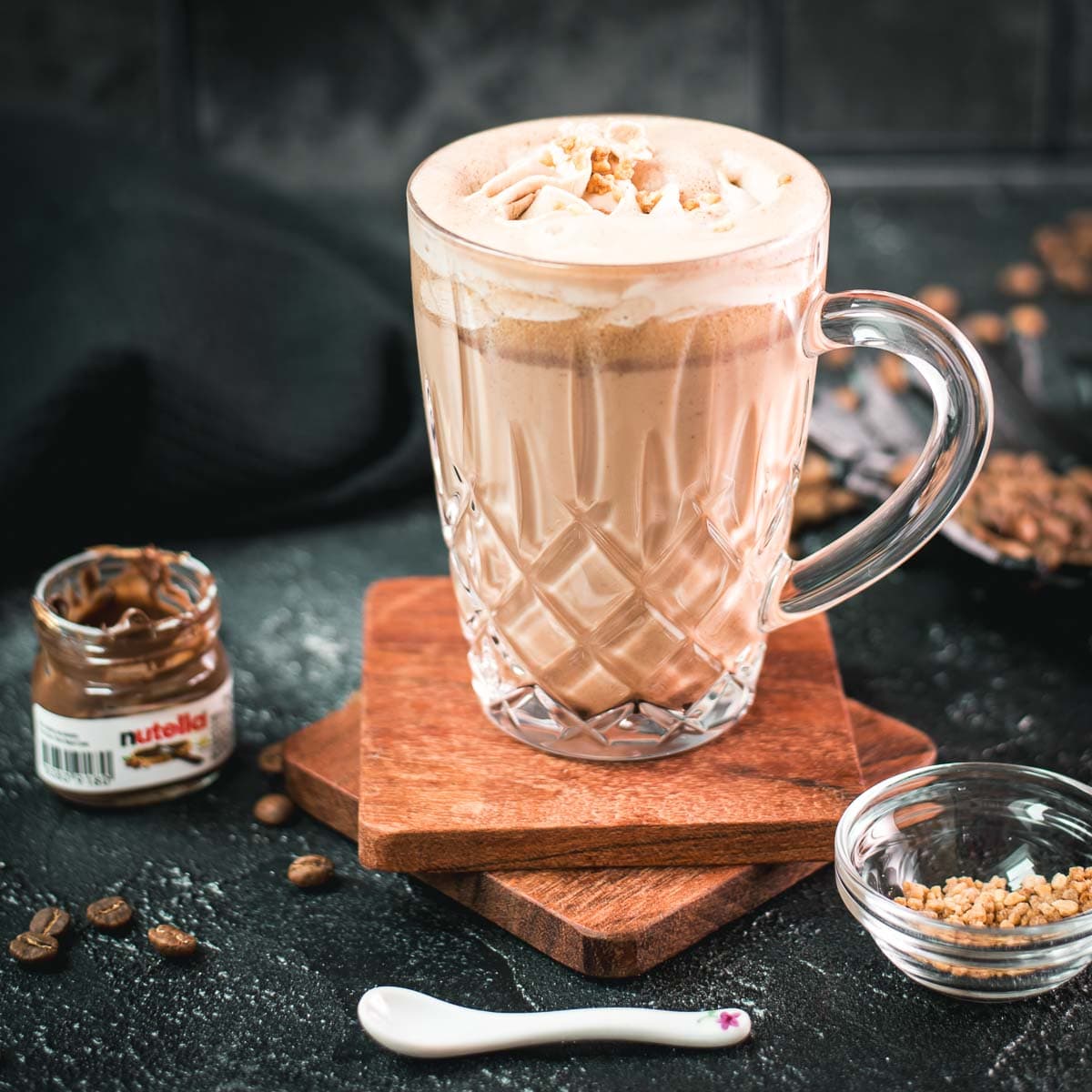 Divine Nutella coffee with homemade Nutella-flavored whipped cream, placed on two wooden coaters on dark ground.