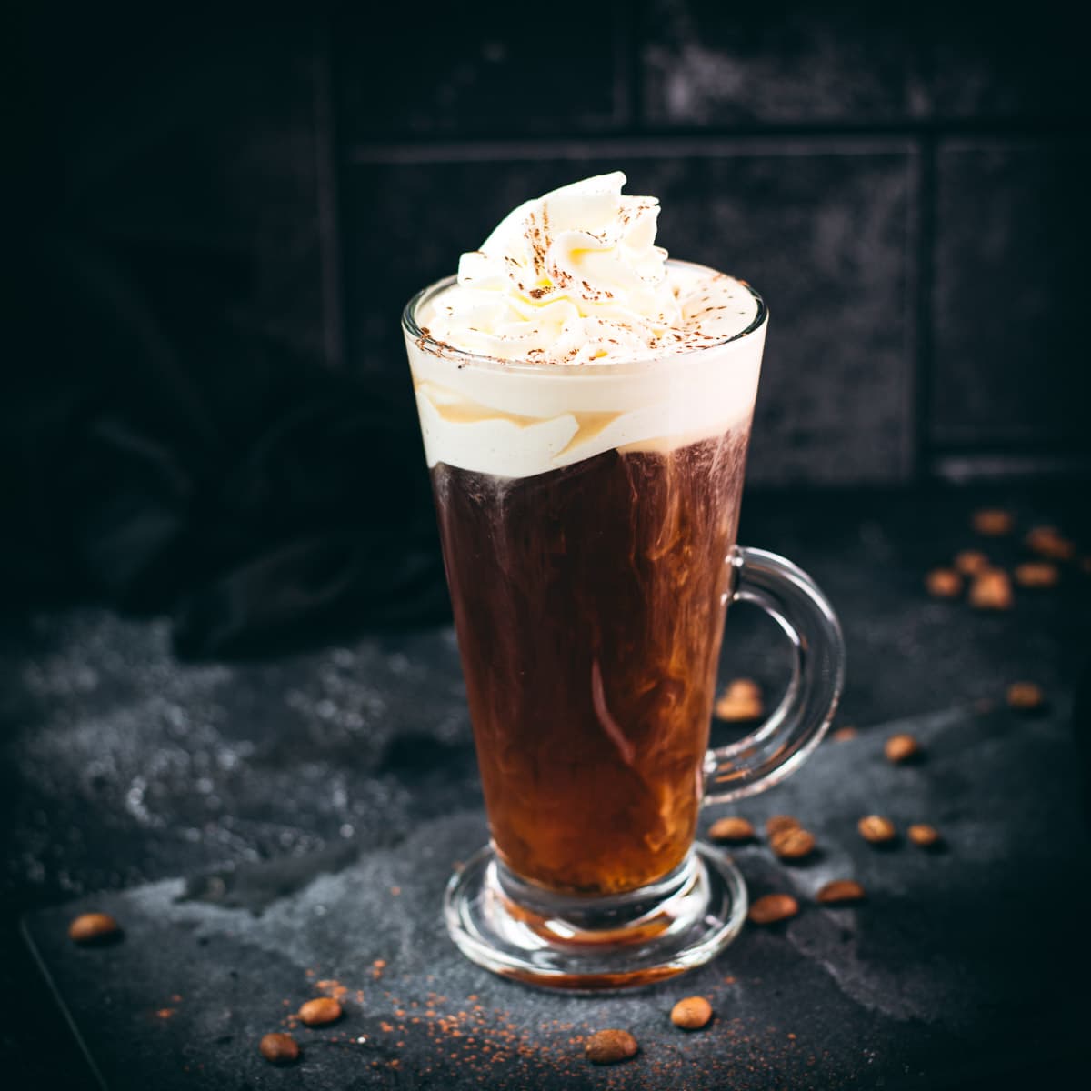 Delicious Irish coffee, topped with whipped cream and sprinkled with cocoa powder, placed on black slate plate.