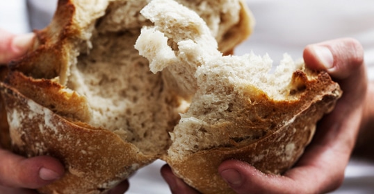 Hands tearing a freshly baked, artisanal loaf of crusty bread in half, revealing the soft interior, is truly an art.