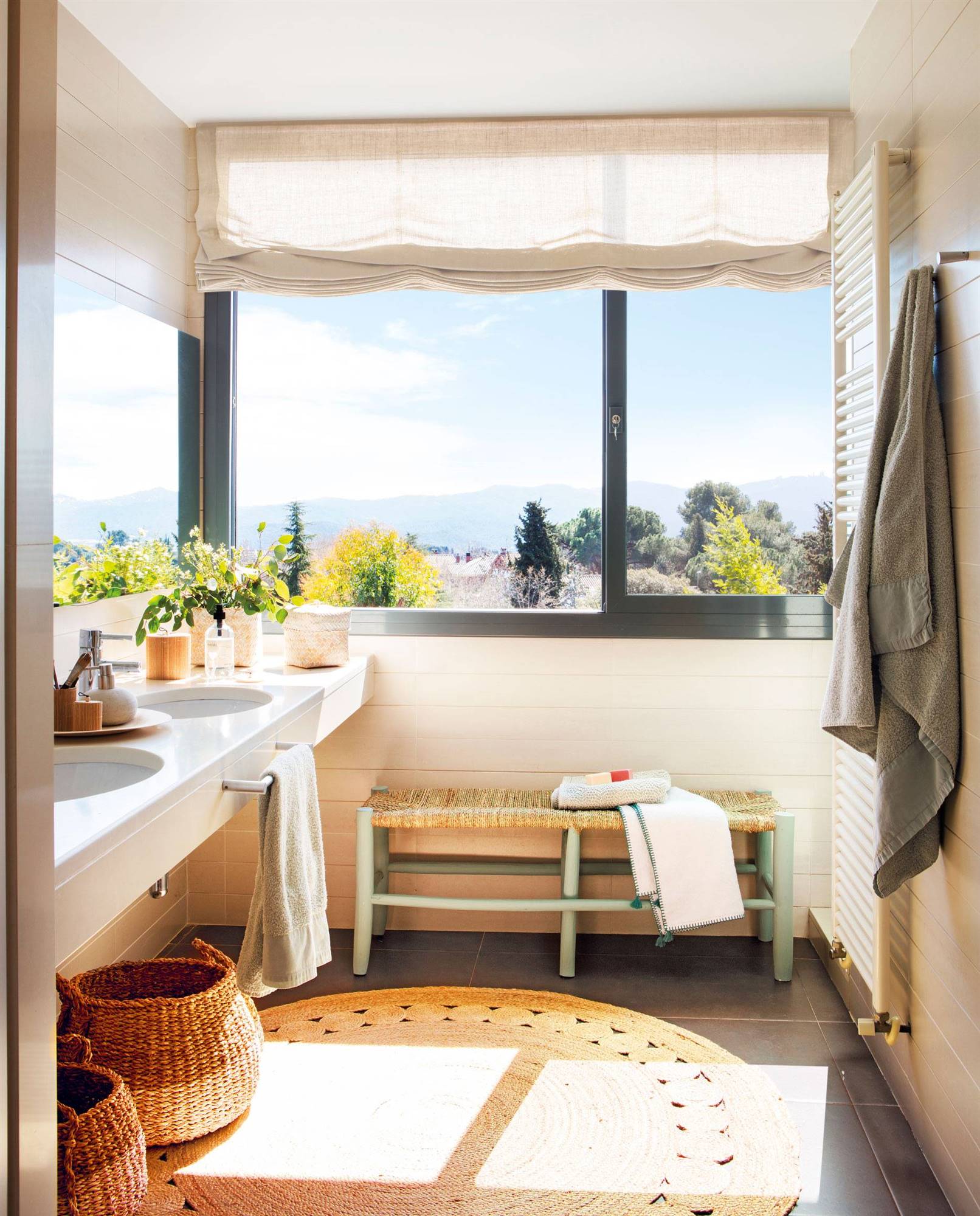 Baño con banco y alfombra de fibras naturales, y ventana gris. 