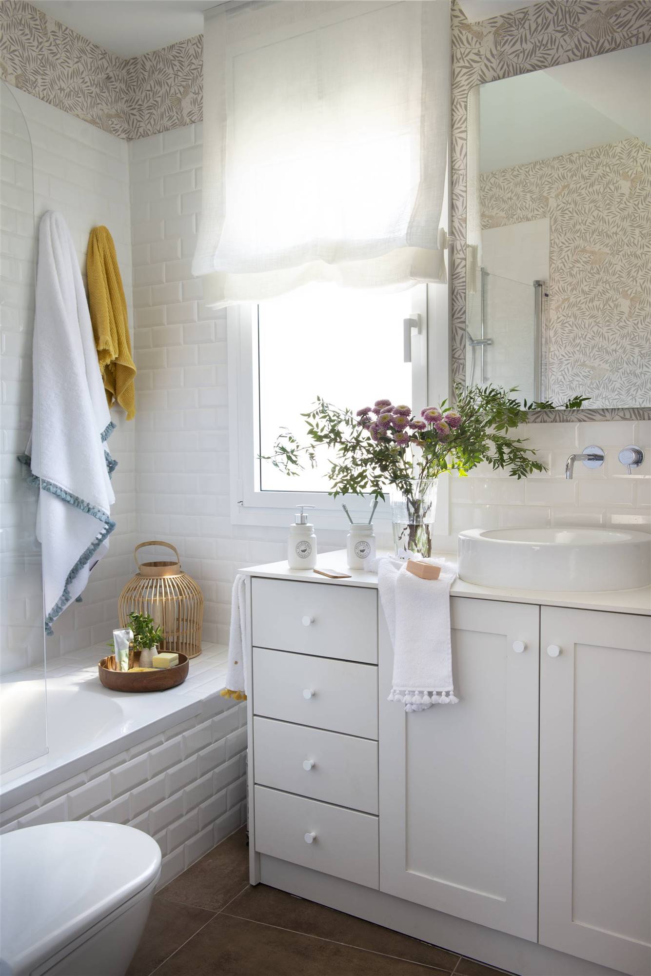 Baño con mueble blanco, papel pintado, azulejos y estor de tela. 