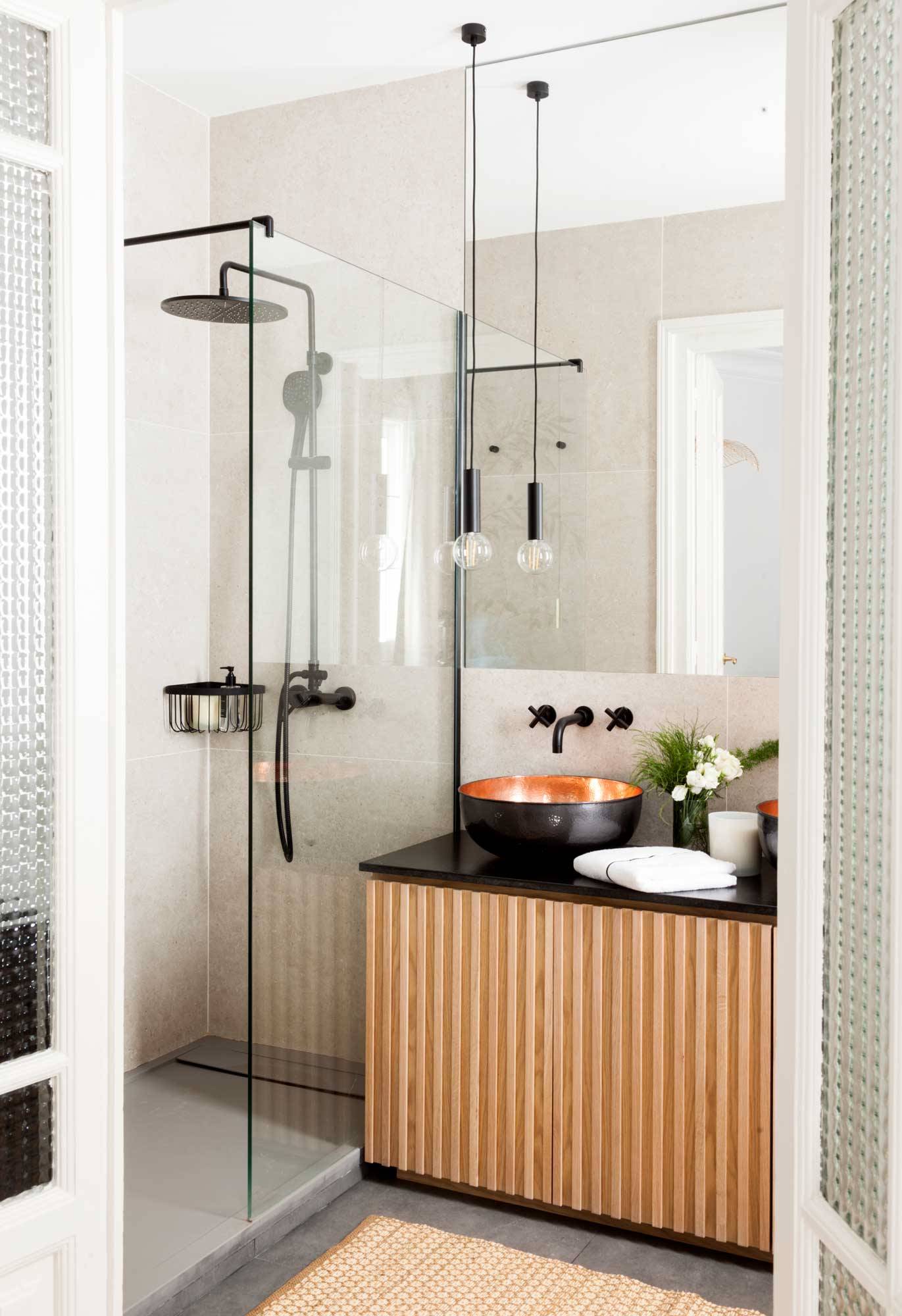 Baño pequeño con mueble moderno, mampara de cristal y lámpara colgante. 