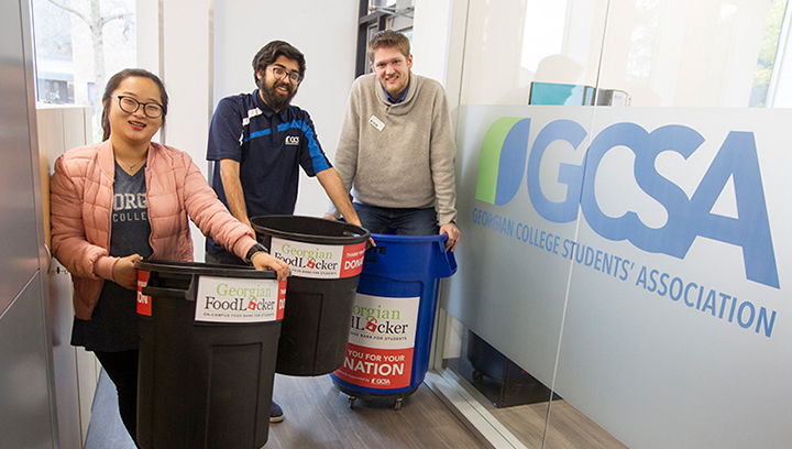 Three people in the GCSA office holding Georgian FoodLocker donation bins