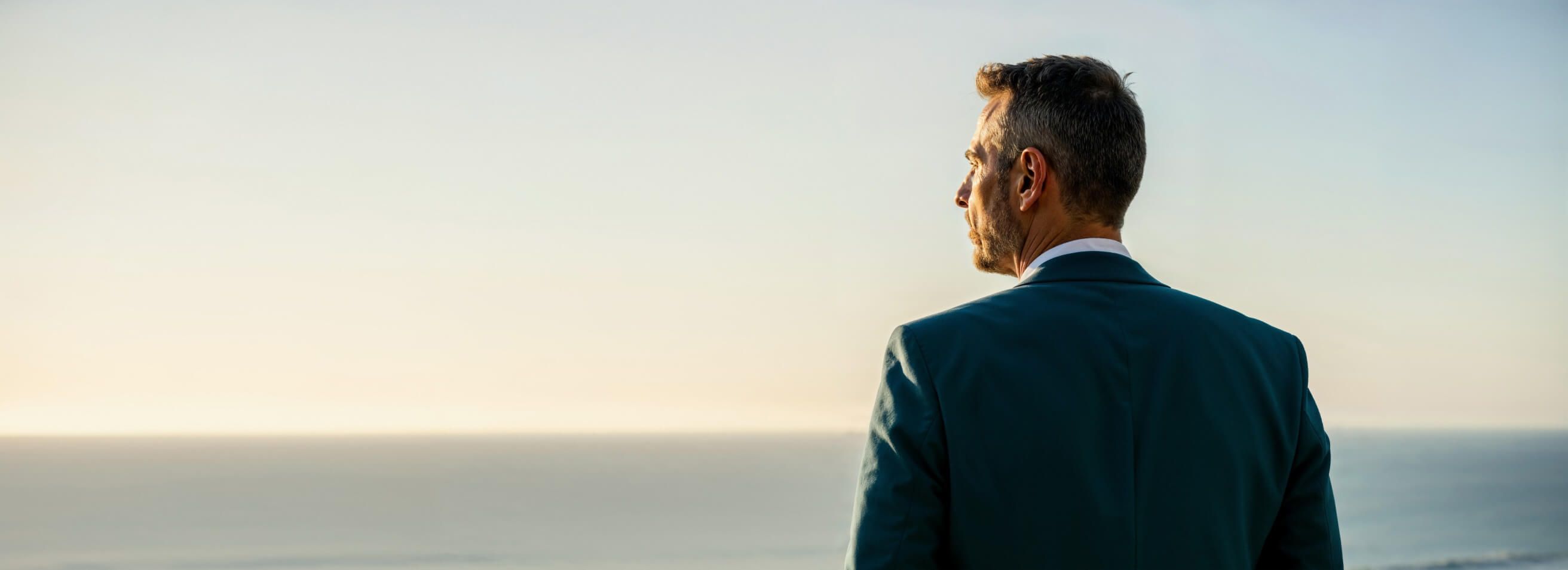 Man in a suit looking out at the sea.