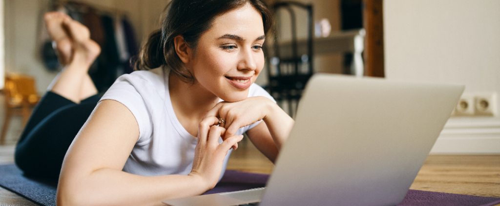 Beautiful woman laying on stomach and watching live yoga on a laptop