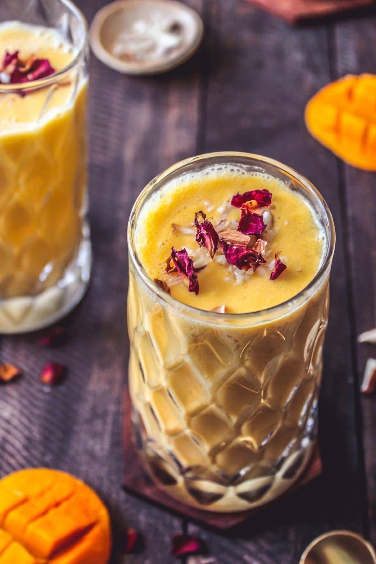 Lassi in glasses with mangoes on table beside them