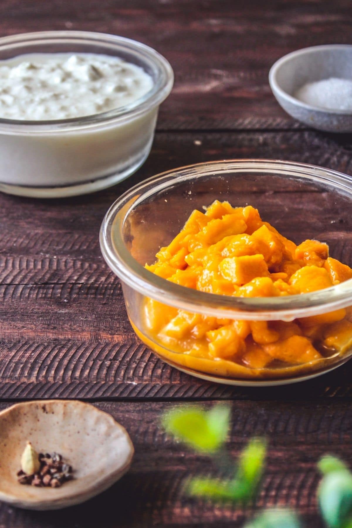 Ingredients for mango lassi in glass bowls on wood table