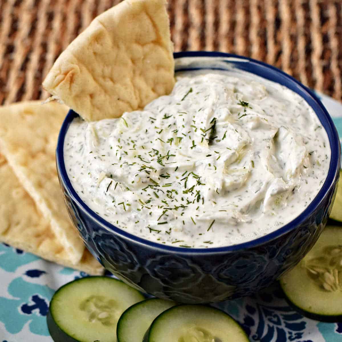 Cucumber and yogurt dip in a small bowl with pita chips and sliced cucumber.