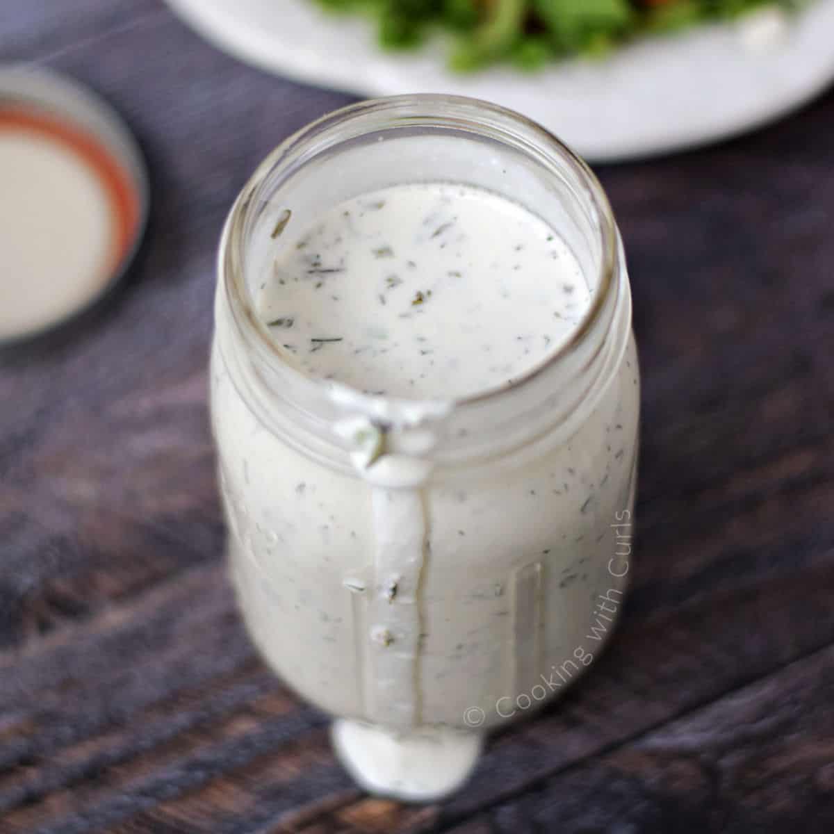 Creamy feta dressing in a mason jar with a Greek salad in the background.