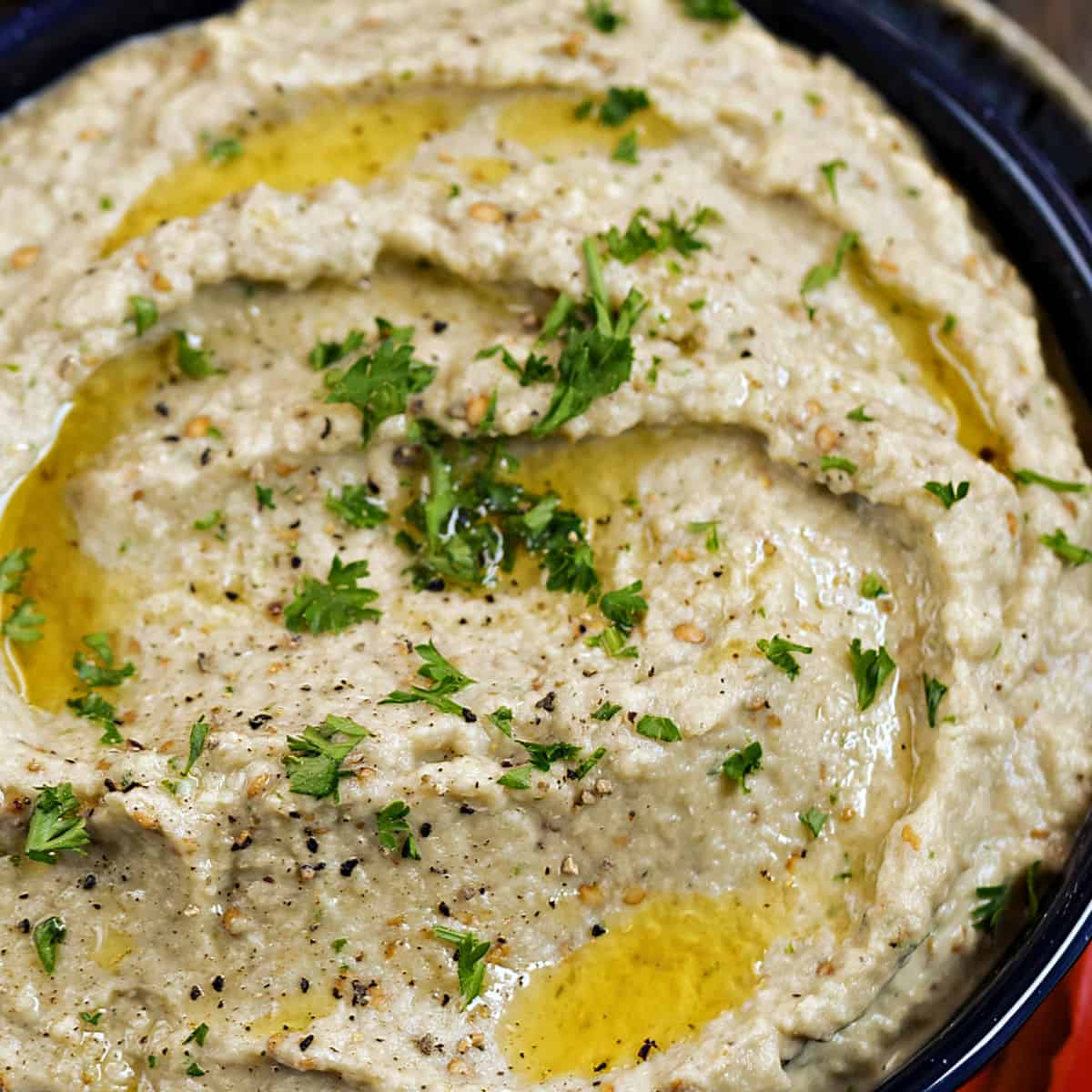 Looking down on a bowl of roasted Greek Eggplant Dip drizzled with olive oil and sprinkled with chopped parsley.