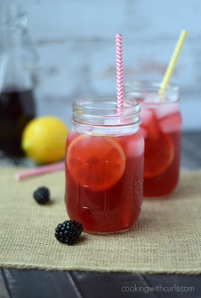 Blackberry Passion Tea Lemonade in glass mason jars with colorful paper straws and a lemon in the background