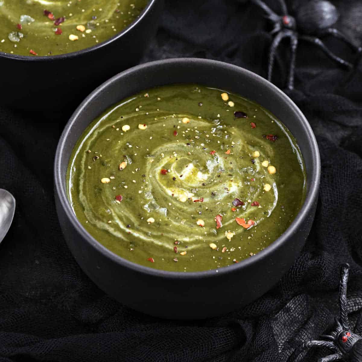 Two black bowls filled with deep green soup with cream swirled through the centers.