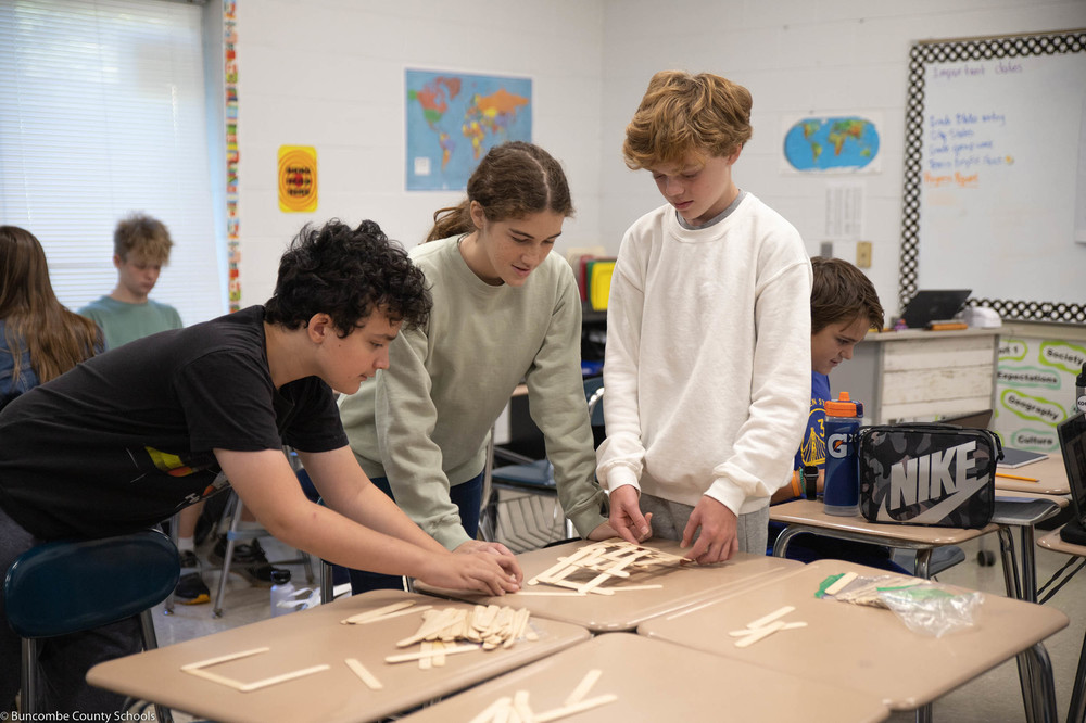 Students working in a group to build a bridge with popsicle sticks.