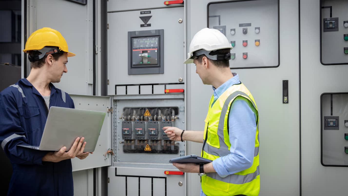 Two electricians monitor a large electrical system