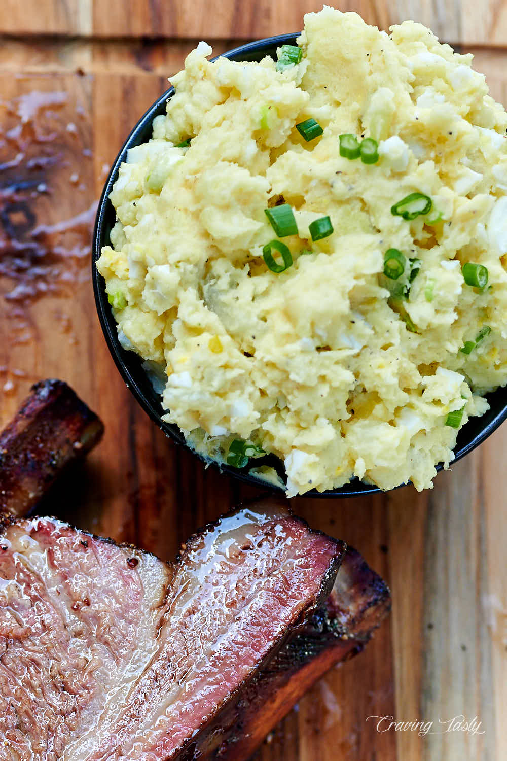 A bowl of southern potato salad next to smoked beef ribs.