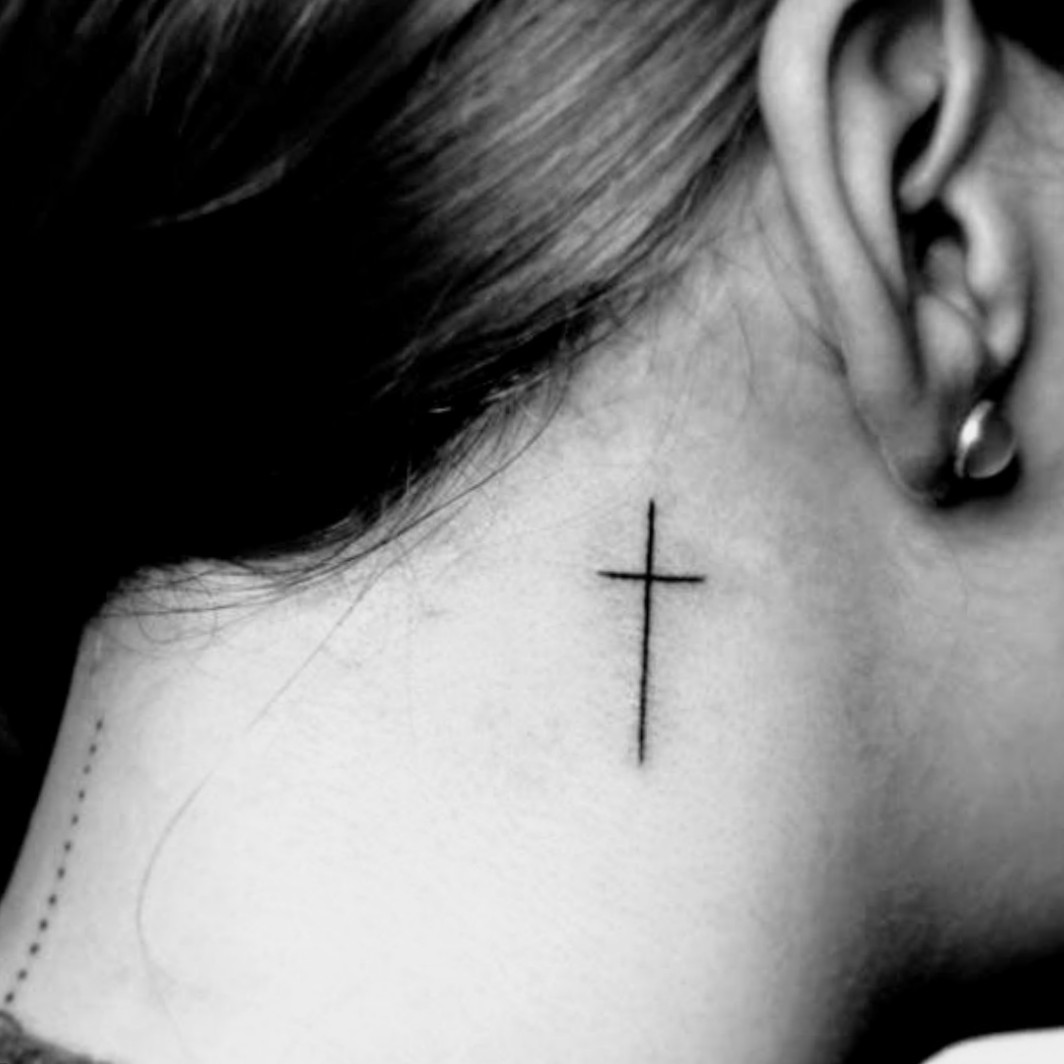 Minimalist cross tattoo behind the right ear