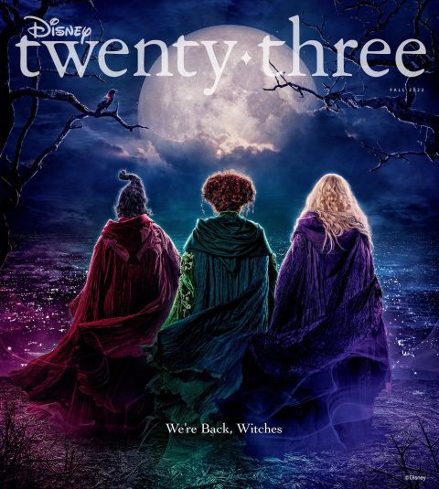 The front cover of Disney twenty-three, featuring the publication logo above the backs of Sarah, Winnifred, and Sarah Sanderson, all wearing cloaks and standing on a wooded hill overlooking a town at night. The text below them states, “We’re back, witches.”