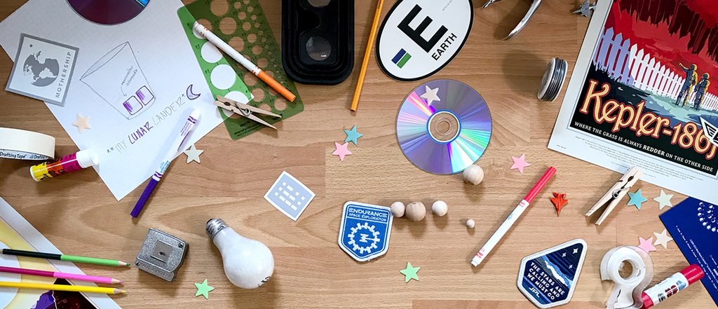 Office supplies, craft materials, space stickers and other objects strewn across a wood floor.