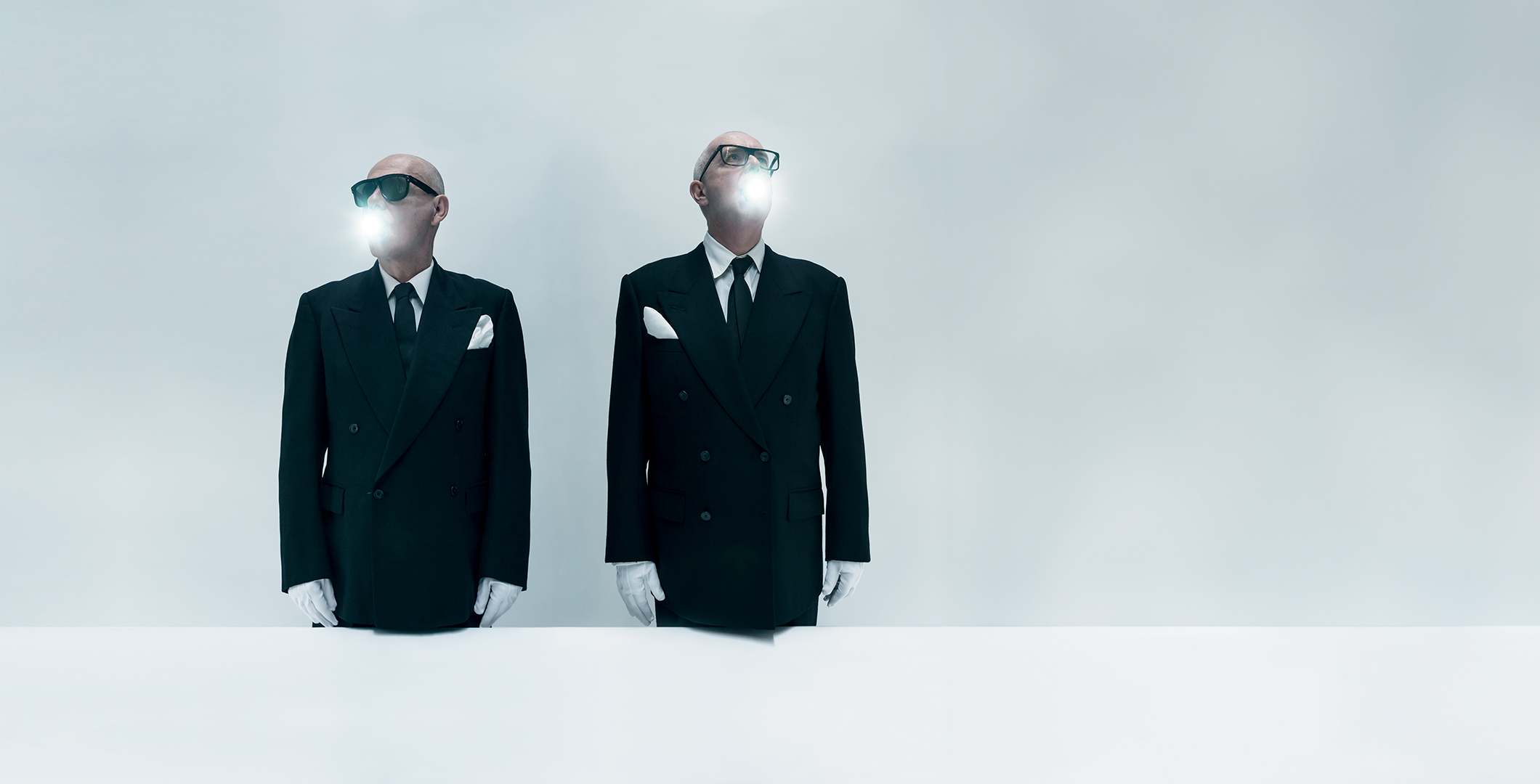 Chris Lowe and Neil Tennant in black suits and sunglasses with light coming out of their mouths