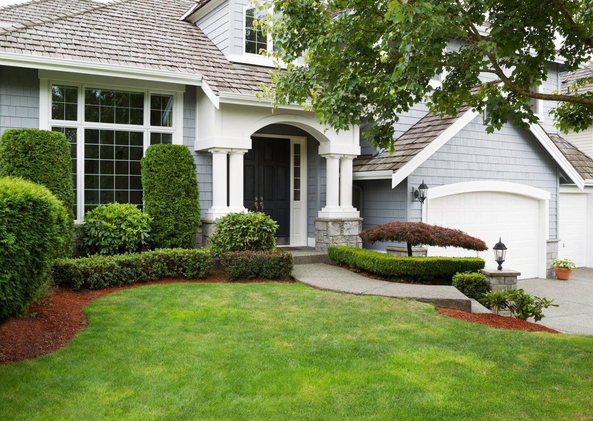 Exterior of beautiful baby blue home with green grass and flower beds.