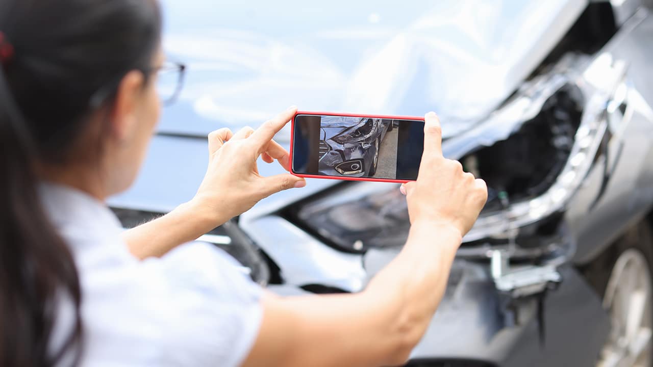 Woman agent takes pictures of damage to car after accident by smartphone