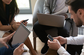 Group of four with devices huddled and brainstorming