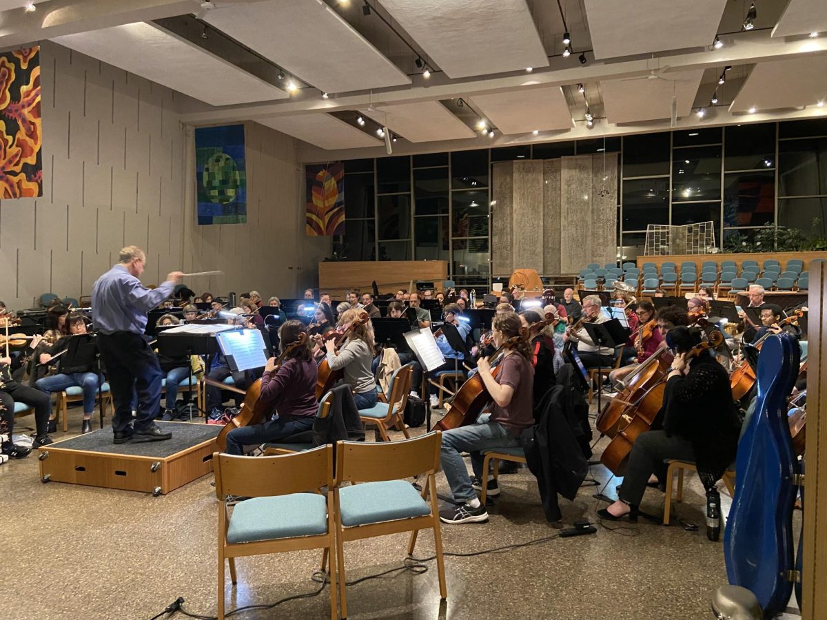 Around 90 orchestra members gather in a semicircle around Music Director and conductor Lawrence Eckerling.