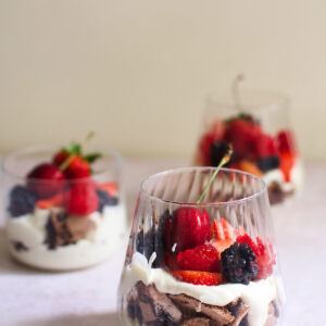 A glass of chocolate eton mess with cherries, strawberries, raspberries, and blackberries.