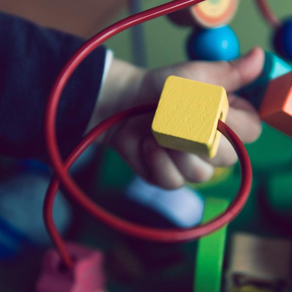 baby's hand moves a yellow block along a red spiral wire