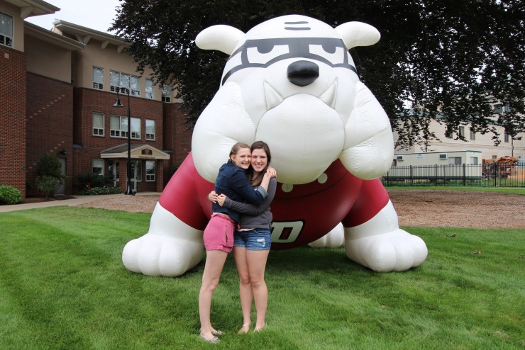 Two students standing outside hugging in front of a blow-up bulldog on the lawn of woodward hall