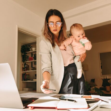 O mamă care ține copilul în brațe și lucrează la laptop