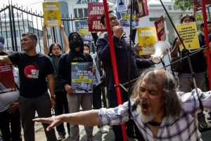 A man stands before a crowd, holding a sign to protest