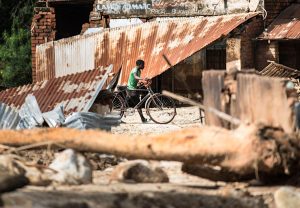 A person pushes a bicycle past damaged structures