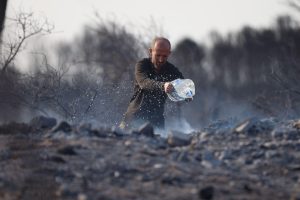 man throwing water from large plastic bottle onto charred area