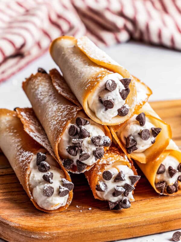 Six cannolis forming a pyramid on a cutting board with a kitchen towel in the background.