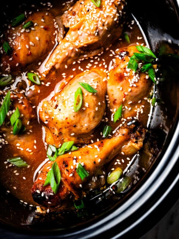 Crock pot chicken drumsticks garnished with sesame seeds and green onions inside the slow cooker.