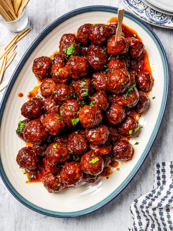 Overhead view of a platter of grape jelly meatballs next to a small glass of cocktail toothpicks.