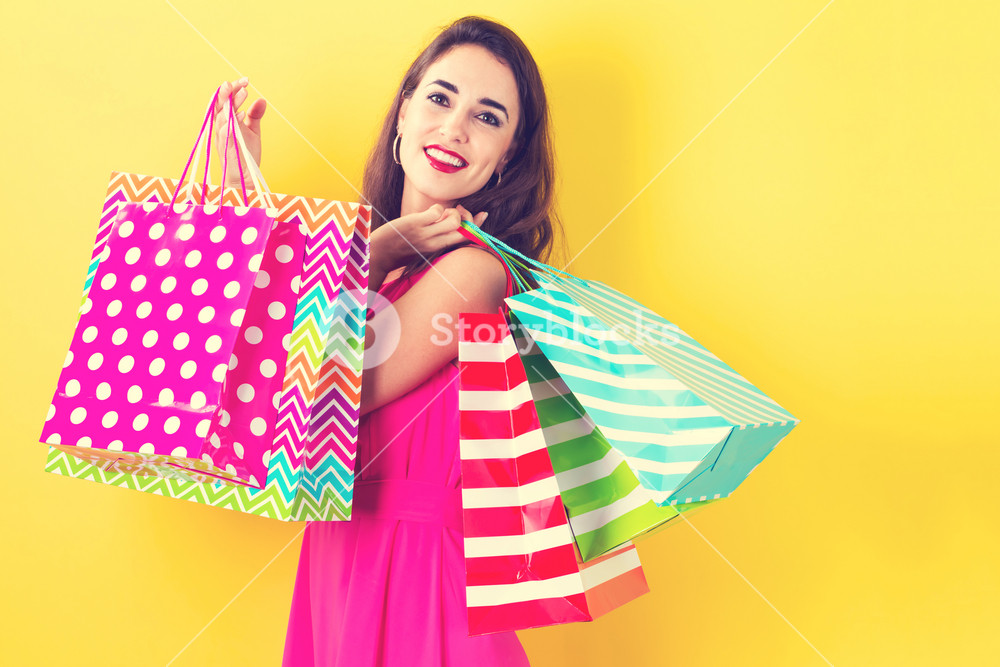 Happy young woman holding many shopping bags on a yellow background  Royalty-Free Stock Image - Storyblocks