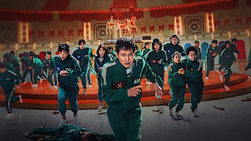 Squid Game season 2 cast in green tracksuits running in a large, decorated room with a carousel in the background, appearing intense and determined.