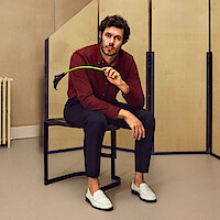 Adam Brody sits on a stool holding a black calla lily