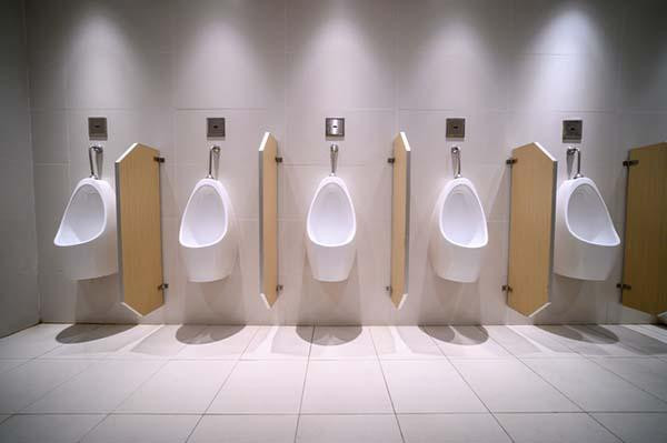 A row of urinals in a public restroom, with light-colored dividers between them.