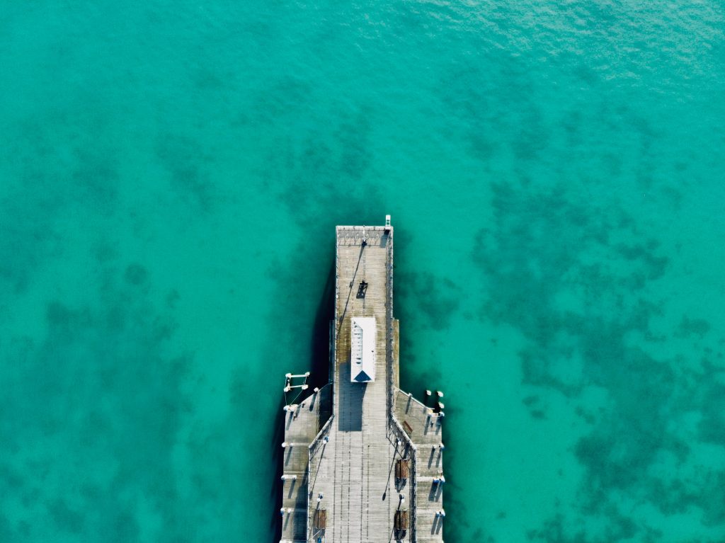 Birds eye view drone shot of Swanage Pier in Dorset, the end of a wooden pier surrounded by bright cyan water on a very sunny day