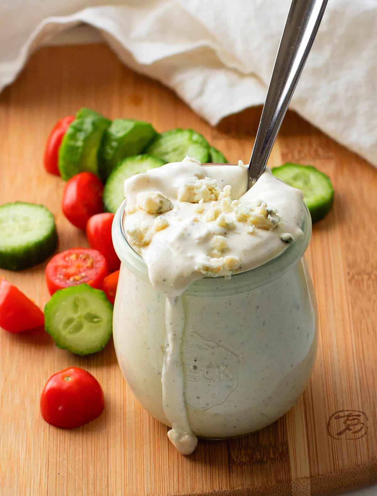 Blue Cheese Dressing in a glass jar with sliced tomatoes and cucumbers